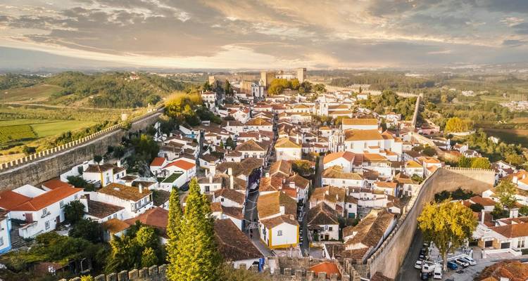 Vista aérea de una ciudad medieval con una muralla que la rodea al atardecer.