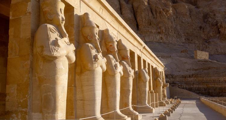 Rangée de statues massives de pharaons en grès gardant la façade d'un temple égyptien antique sous la lumière du désert.