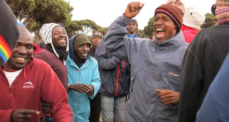 Vrolijke groep trekkers en gidsen die lachen en dansen in berguitrusting voor buiten.