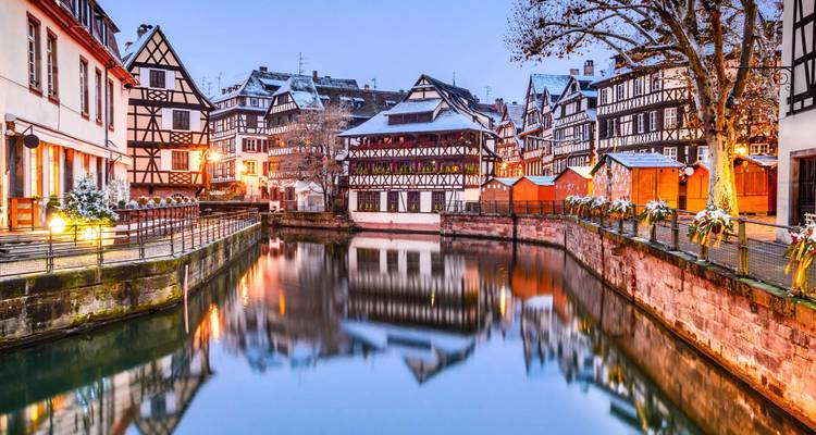Met sneeuw bestoven vakwerkhuizen die reflecteren in een rustige gracht bij schemering in Straatsburgs Petite France.