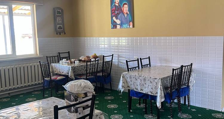 Zone de restauration modeste avec plusieurs tables, tapis vert à motifs et murs carrelés lumineux.