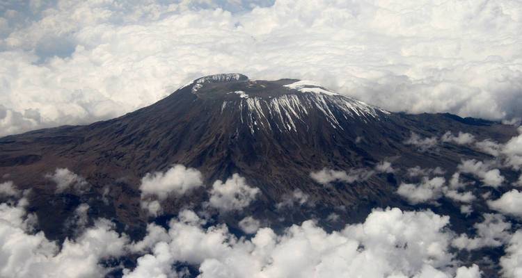 Vista aérea de la cumbre del Monte Kilimanjaro emergiendo a través de un mar de nubes con franjas de nieve