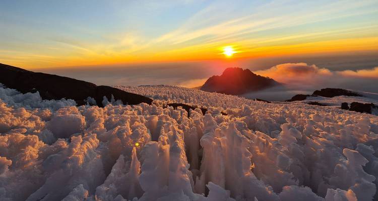 El amanecer sobre el Kilimanjaro iluminando formaciones de hielo cristalino puntiagudo con una luz dorada cálida