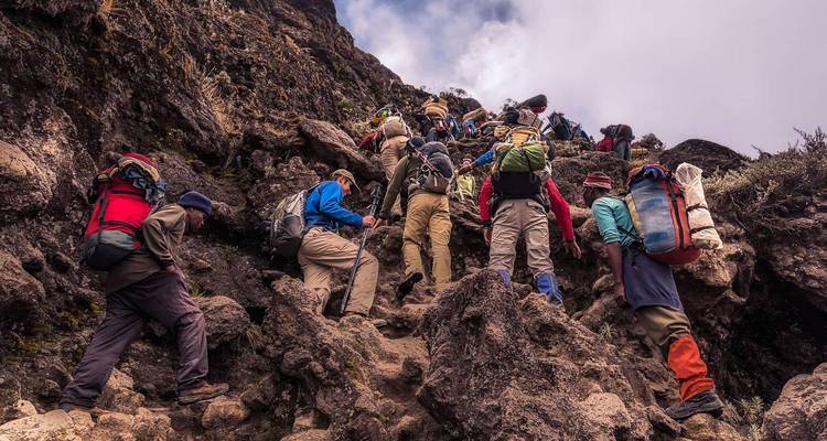 Un gran grupo de excursionistas subiendo rápidamente por un sendero rocoso en el Monte Kilimanjaro llevando mochilas