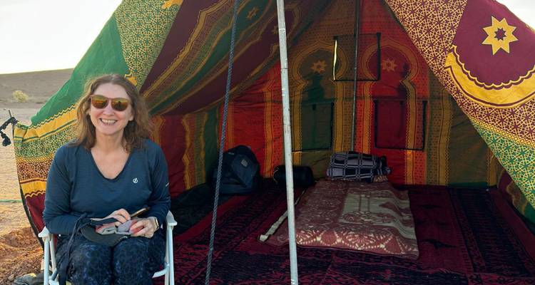 Une femme souriante devant une tente colorée dans le désert.