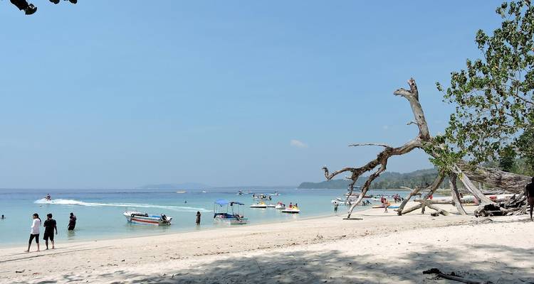 Ein weißer Sandstrand mit Menschen und Booten in klarem blauen Wasser.