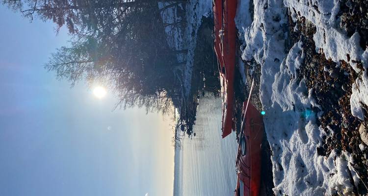 Kayaks sur un rivage enneigé au bord d'un lac calme avec le soleil bas dans le ciel.