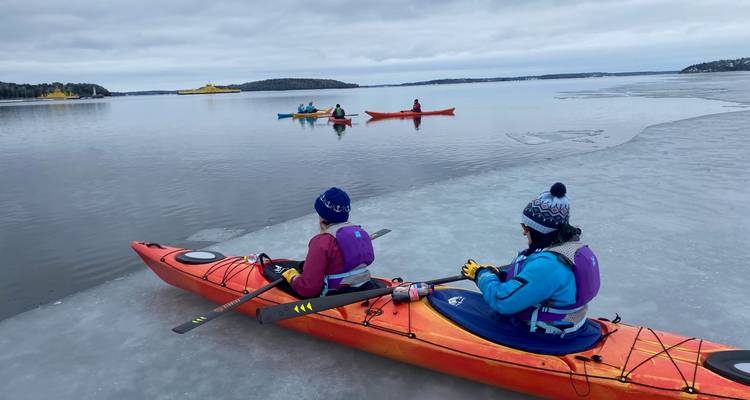 Groupe de kayakistes pagayant sur un lac glacé et calme.