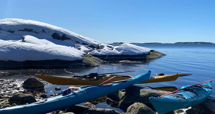 Colorful kayaks pulled onto a snowy granite shoreline overlooking calm blue sea of an archipelago