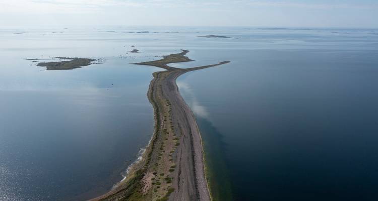 Imagen de dron de una delgada calzada de grava que serpentea a través de un vasto mar tranquilo con pequeños islotes a la distancia.