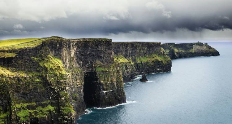 Falaises spectaculaires de Moher avec des vagues de mer qui se brisent en contrebas sous un ciel nuageux.
