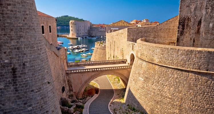 Murallas de piedra históricas y puente del casco antiguo de Dubrovnik junto al agua.