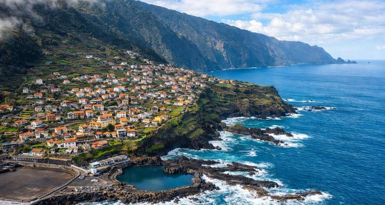 Un village côtier en terrasses perché sur des falaises escarpées surplombe les vagues déferlantes de l'Atlantique et une piscine naturelle creusée dans la roche.