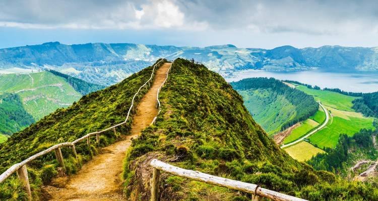 Un sentier de terre avec des garde-corps en bois mène le long d'une crête verdoyante dominant le lac de caldeira de Sete Cidades.