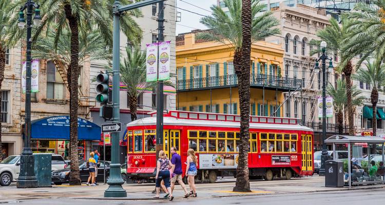 Tranvía rojo brillante pasa por avenida bordeada de palmeras con peatones y edificios históricos en Nueva Orleans.