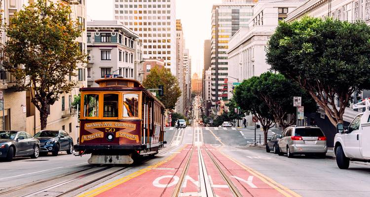 Clásico tranvía de San Francisco subiendo por una empinada calle de la ciudad bordeada de edificios históricos y modernos.