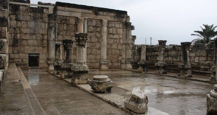 Rain-soaked floor of an ancient limestone synagogue with standing columns and carved capitals.