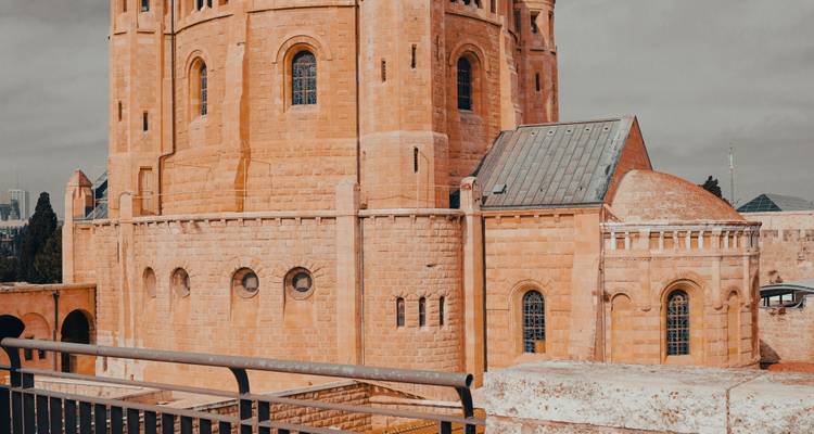 Sandstone abbey with circular apse and narrow windows seen from terrace railing.
