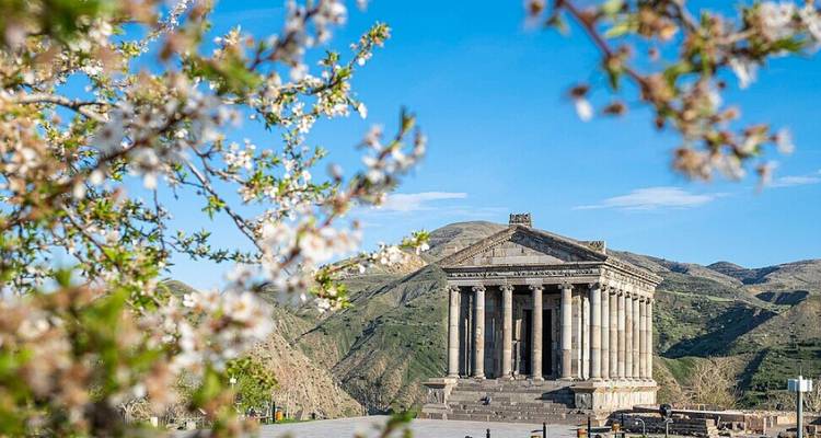 Tempel von Garni inmitten von Frühlingsblüten mit grünen Hügeln und blauem Himmel im Hintergrund.