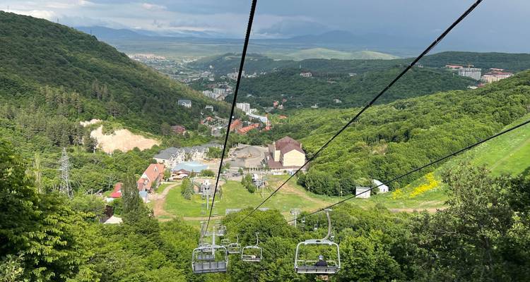 Blick von einem fahrenden Sessellift, der über üppig grüne Hügel und verstreute Gebäude hinabfährt.