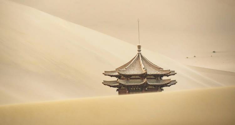 A traditional pagoda partially obscured by sand dunes.