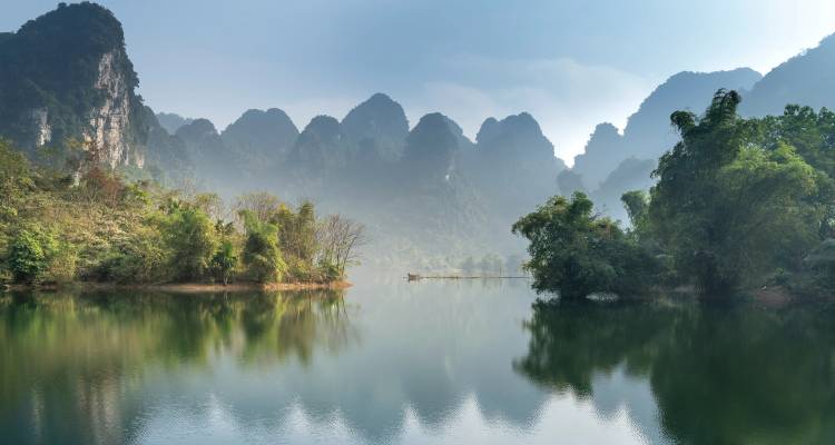 Lac pittoresque entouré de pics karstiques boisés sous un ciel dégagé.