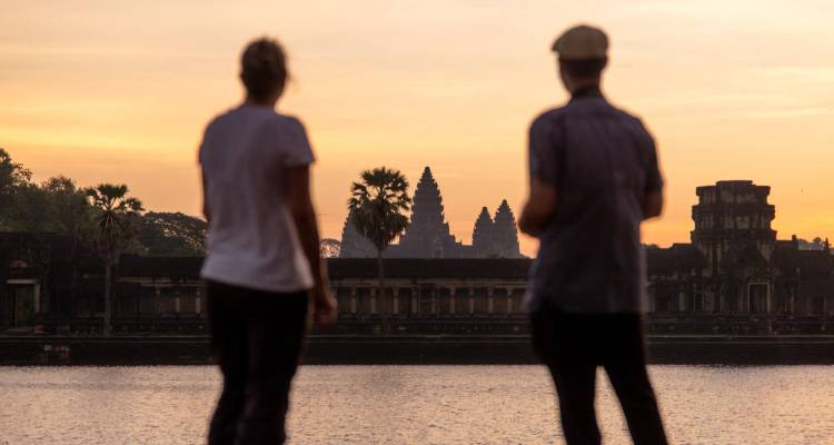 Deux voyageurs observent le lever du soleil au-dessus du bassin de réflexion avec les tours d'Angkor Wat en silhouette dans le lointain.