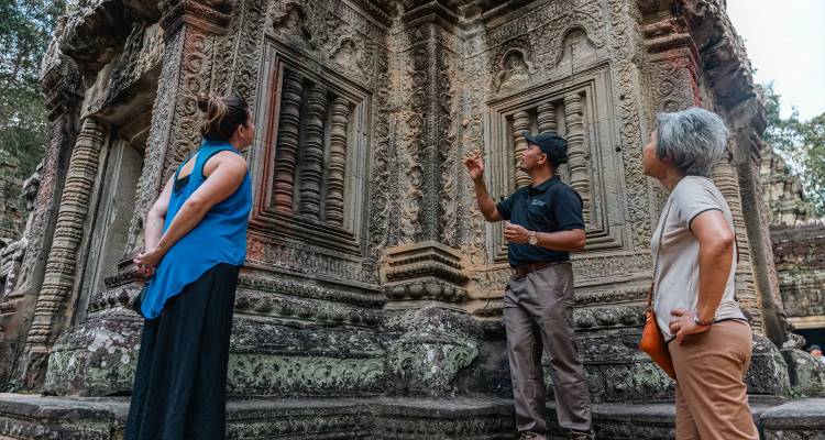 Le guide explique les sculptures en bas-relief complexes aux visiteurs dans un temple cambodgien ancien.