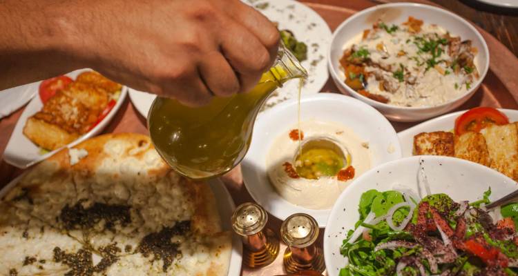 Assortierte nahöstliche Mezze-Gerichte mit Olivenöl, das über cremigem Hummus gegossen wird.