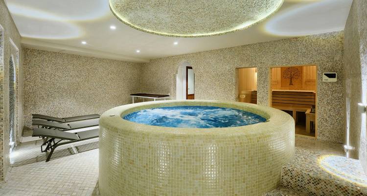 Luxuriöses Indoor-Spa mit rundem Whirlpool, Liegestühlen und Wänden mit Mosaikfliesen