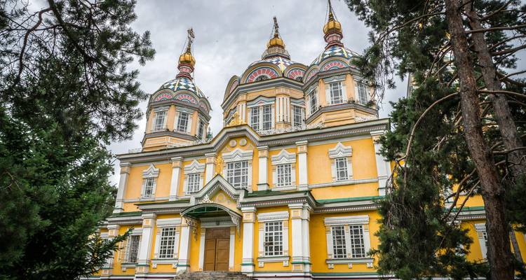Farbenfrohe hölzerne orthodoxe Kathedrale mit kunstvollen Kuppeln, umgeben von Kiefernbäumen.