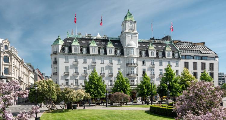 Historisch wit hotel met groen koperen dak en Noorse vlaggen naast een aangelegde stadspark.