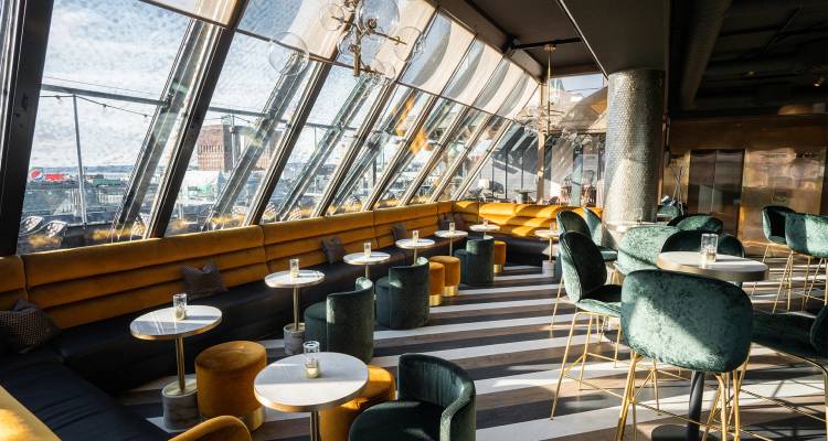 Stijlvolle rooftopbar met schuine glazen wanden, fluwelen zitplaatsen en uitzicht op de haven.