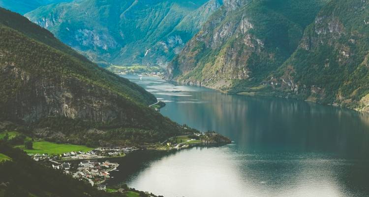 Rustige fjord die zich tussen steile beboste bergen slingert met een klein dorpje aan de waterkant.
