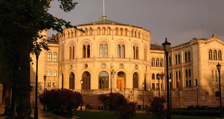 Het Stortinget-parlementsgebouw verlicht door warm licht tegen een sombere lucht.