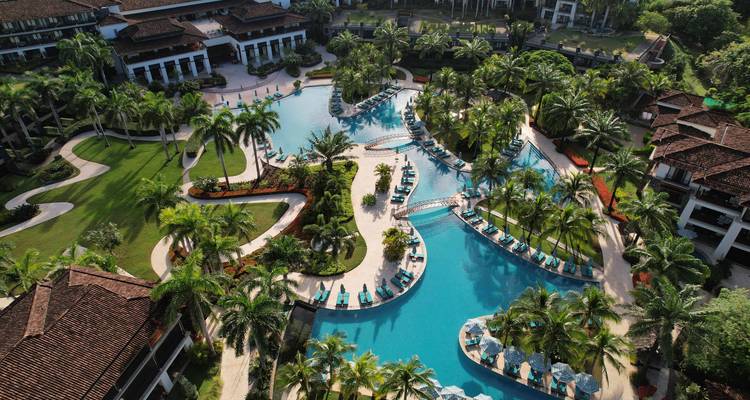 Vue aérienne d'un complexe de piscines de style lagon expansif au milieu d'un aménagement paysager tropical.