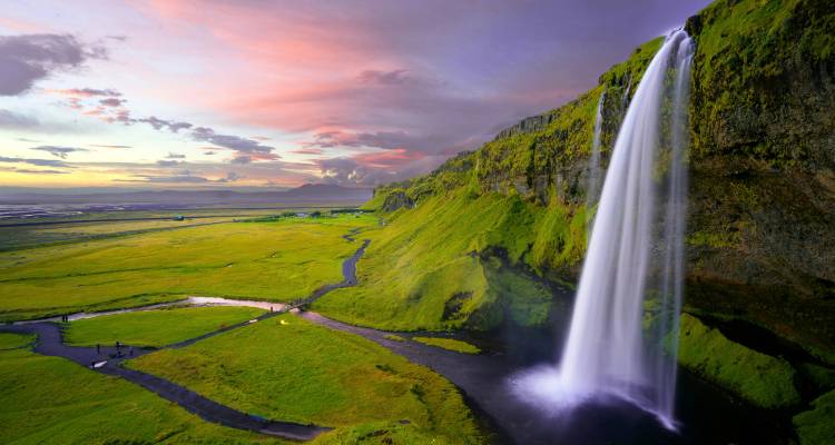 Une cascade majestueuse dévalant une falaise dans une vallée luxuriante sous un ciel aux belles couleurs.