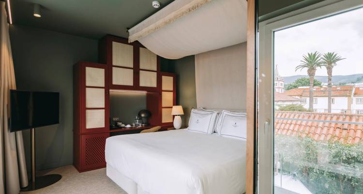 Chambre d'hôtel lumineuse avec lit à baldaquin et vue sur les toits carrelés et les palmiers.
