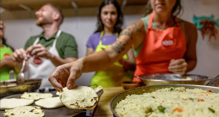 Les participants du cours de cuisine préparent des plats traditionnels et présentent une tortilla fraîchement faite à la caméra.