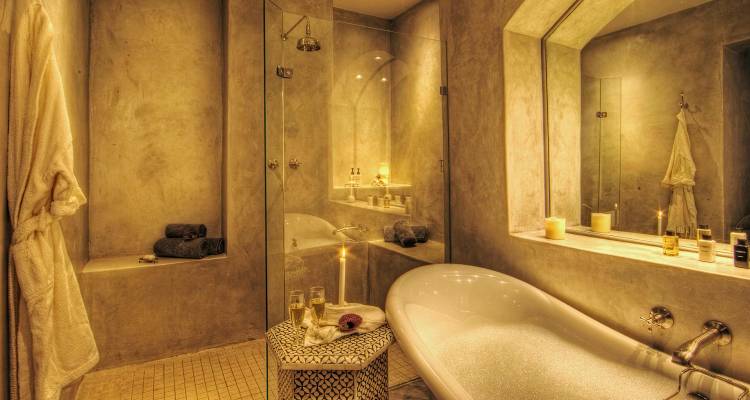 Elegant spa-like bathroom with freestanding tub, candles and champagne on a stool.