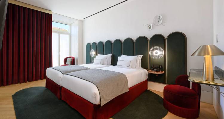 Habitación de hotel con dos camas individuales y muy luminosa, paneles de cabecero en verde esmeralda, base roja, una ventana grande con cortinas e iluminación suave