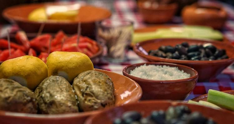 Primer plano de ingredientes tradicionales de comida en platos de barro, incluyendo limones, papas, aceitunas y sal gruesa