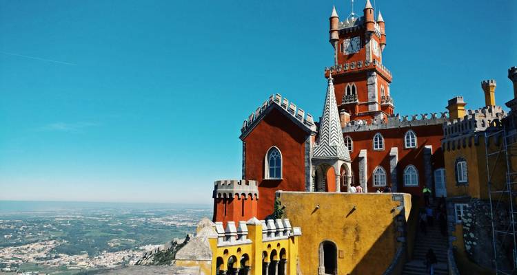 Palacio de Pena vibrante en rojo y amarillo encaramado en la cima de una colina con una amplia vista del campo bajo un cielo azul despejado