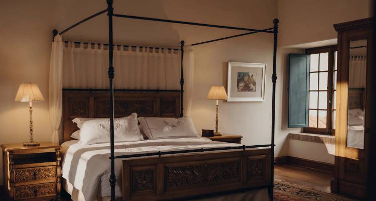 Cálida y elegante habitación de hotel con una cama con dosel de madera tallada, iluminación suave con lámparas y muebles clásicos.