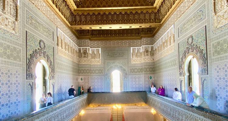 Interior de un salón ricamente decorado con visitantes en los balcones.