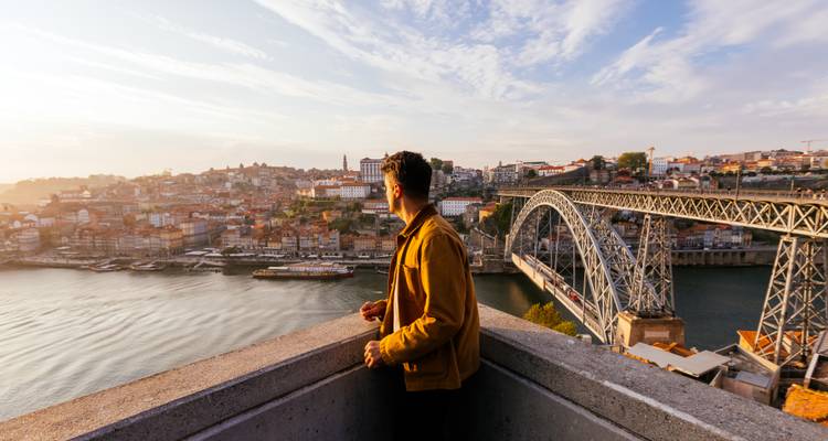 Reisender blickt bei Sonnenuntergang von einer hohen Terrasse über Porto und die Dom Luís I Brücke.