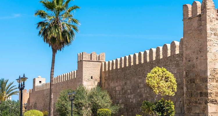 Mur de grès crénelé bordé de palmiers de la médina de Sousse sous un ciel bleu éclatant.