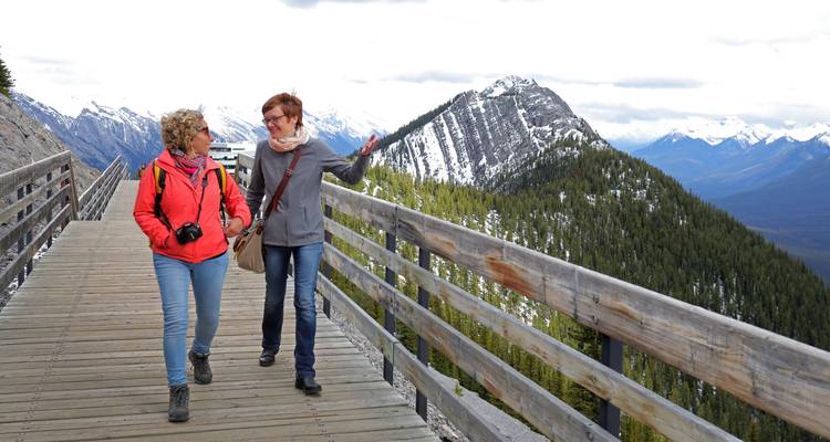 Deux femmes marchant le long d'une promenade en bois avec des sommets enneigés qui s'élèvent derrière elles