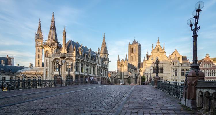 Puente de adoquines que conduce a las ornamentadas torres medievales y agujas del centro histórico de Gante al amanecer.