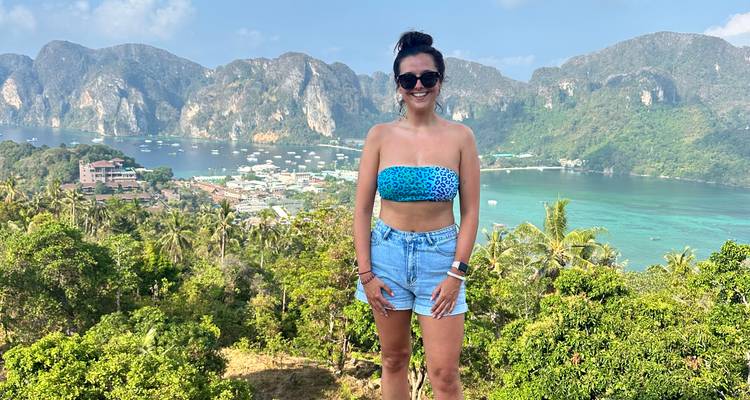 Reisender lächelt an Inselaussichtspunkt mit Blick auf türkisfarbene Bucht, Dorf und Kalksteinfelsen.